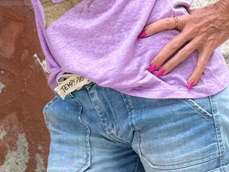 Anti-Aging-Accessoires: Renate Zott mit pink lackierten Nägeln trägt goldene Ringe, lila Shirt und ausgewaschene Jeans mit sichtbarem „Temps des Cerises“-Label. | © Renate Zott