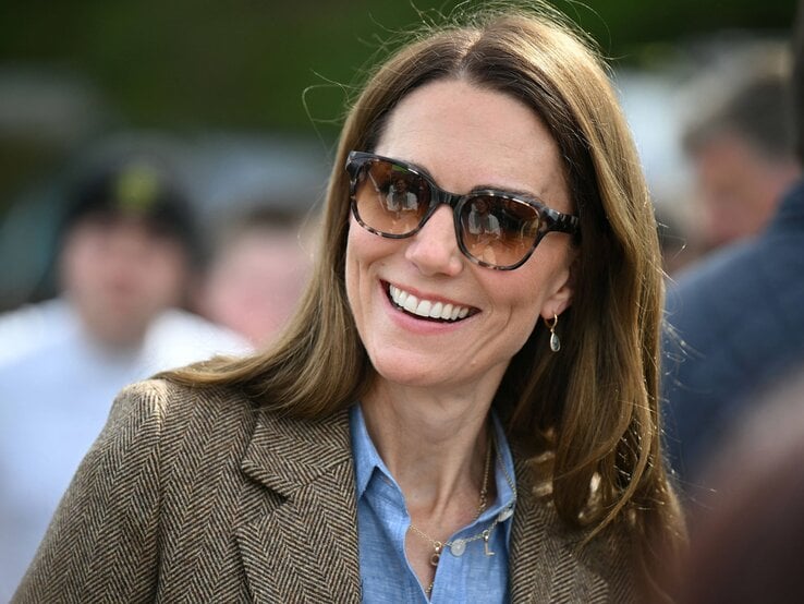 Prinzessin Kate Espadrilles Sandalen Prinzessin Kate mit glatten braunen Haaren, Sonnenbrille und Ohrhänger trägt braunen Blazer über Jeanshemd in sonniger Menschenmenge.