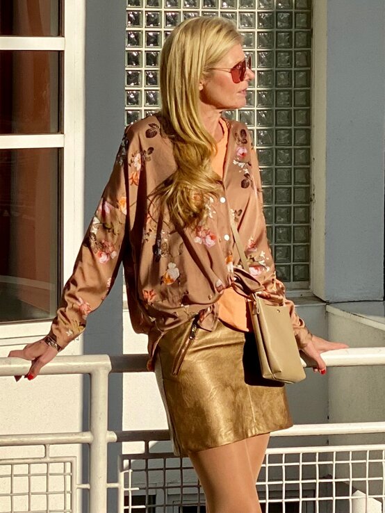 Renate Zott in goldenem Rock und geknoteter Bluse blickt seitlich in die Sonne, Tasche lässig über der Schulter. | © Renate Zott 
