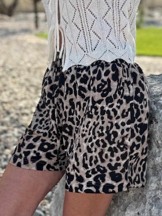 Detailaufnahme einer Frau in sommerlicher Leoparden-Shorts und gehäkeltem Top vor kieseligem Untergrund und grünem Gras. | © Renate Zott