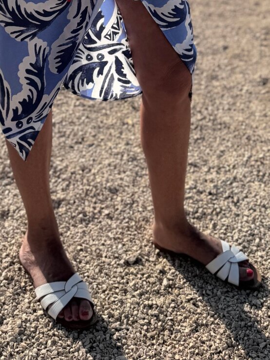 Sommerlicher Look mit luftigem Wickelrock und eleganten weißen Ledersandalen vor einem Untergrund aus kleinen Kieselsteinen | © Renate Zott