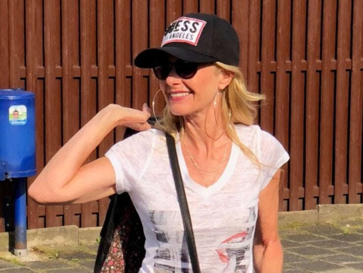 Sommeroutfit mit weißem T-Shirt, schwarzer Tasche mit Aufnähern, Base Cap und einer lässig über die Schulter geworfenen Jacke in der Sonne. | © Renate Zott