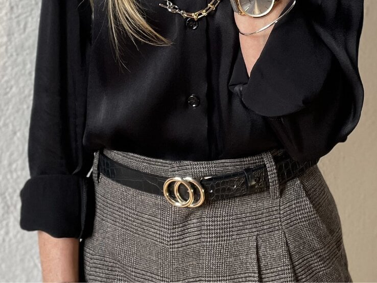 Nahaufnahme eines klassischen Looks mit schwarzer Bluse, grauem Hahnentritt-Muster und einem geprägten Ledergürtel mit goldenen Details. | © Renate Zott