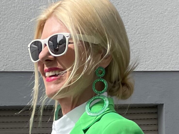 Stilvolles Outfit mit knallgrünem Blazer, weißer Bluse und großen, runden Ohrringen, passend zu einer urbanen Kulisse. | © Renate Zott