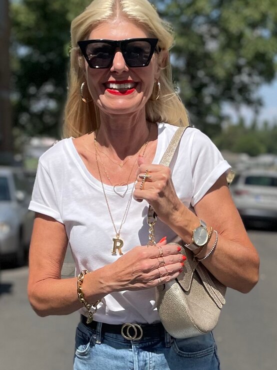 Eleganter Freizeitlook mit weißem Shirt, goldenen Accessoires, einer Gürtel-Schnalle mit Ringsymbol und handlicher Beigetasche. | © Renate Zott