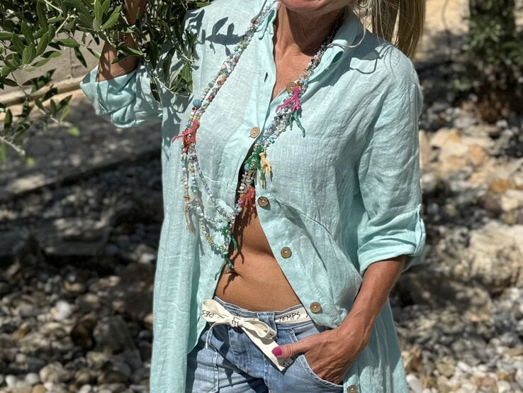 Sommerliches Outfit mit offenem Leinenhemd, kurzen Jeans und verspielten, farbenfrohen Ketten in einer sonnigen Umgebung. | © Renate Zott