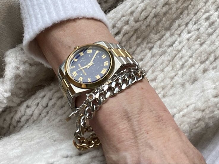 Eine elegante zweifarbige Armbanduhr mit römischen Ziffern, kombiniert mit silbernen und goldenen Armkettchen auf einer cremefarbenen Strickdecke. | © Renate Zott
