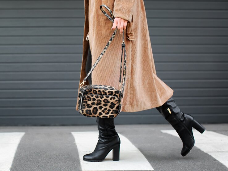 Frau in braunem Cordmantel läuft über einen Zebrastreifen, trägt schwarze Stiefel und eine Tasche mit Leopardenmuster.