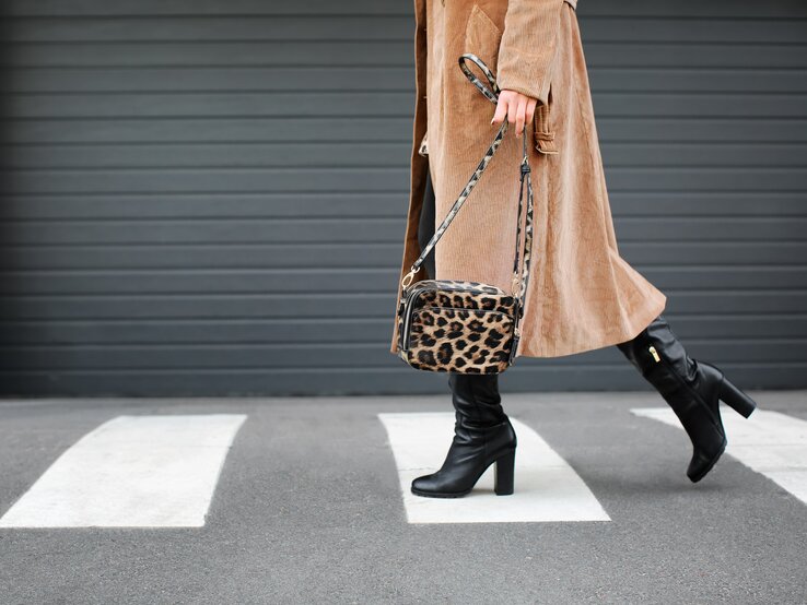 Frau in braunem Cordmantel läuft über einen Zebrastreifen, trägt schwarze Stiefel und eine Tasche mit Leopardenmuster.