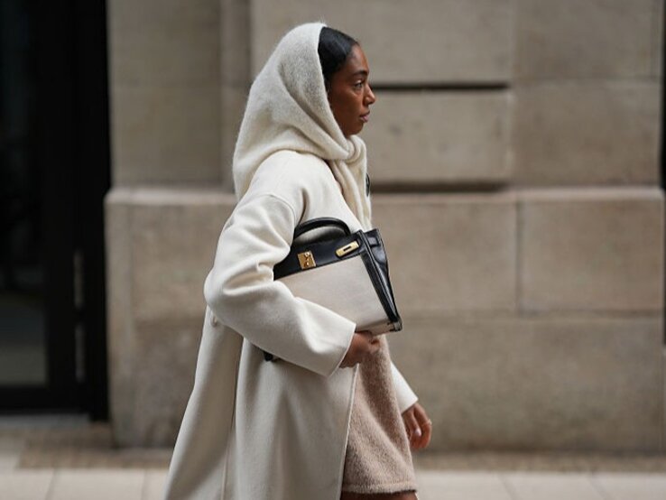 Zu sehen ist eine Frau, die ein beiges Wnteroutfit inklusive Schlupfschal trägt.