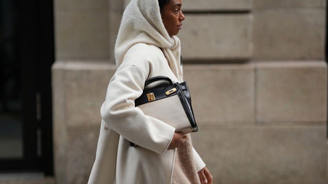 Zu sehen ist eine Frau, die ein beiges Wnteroutfit inklusive Schlupfschal trägt.