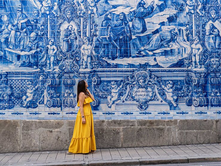 Schöne Frau in gelbem Sommerkleid steht vor Sehenswürdigkeit mit Fließen in Lissabon.