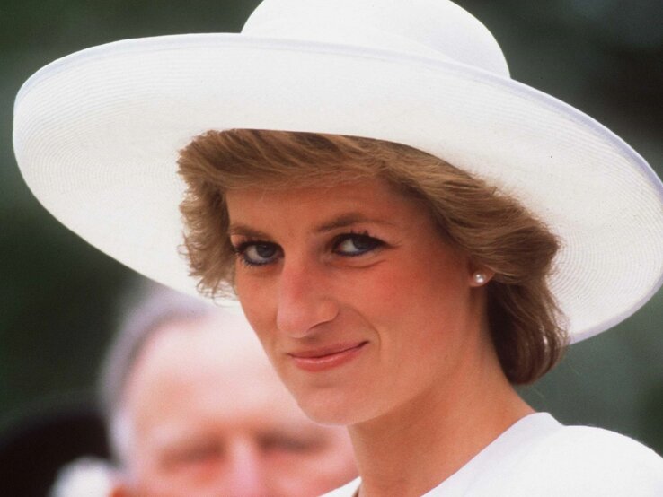 Das Bild zeigt Prinzessin Diana im Jahr 1989 mit ihrem charakteristischen kurzen Haarschnitt, die einen weißen Hut mit breiter Krempe trägt. Sie hat ein freundliches Lächeln und trägt schlichten Schmuck. Prinzessin Diana blickt sanft zur Seite und trägt ein Outfit, das Eleganz und Raffinesse ausstrahlt. Das Bild fängt einen Moment der Ruhe und des Selbstbewusstseins ein, mit einem unscharfen Hintergrund, der die Aufmerksamkeit auf Prinzessin Diana im Vordergrund lenkt.
