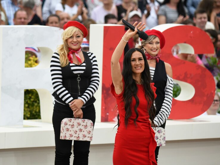 Kiki Cordalis, Tochter von Costa Cordalis, bei einem Auftritt auf einer Bühne. Sie winkt mit einem Mikro in der Hand