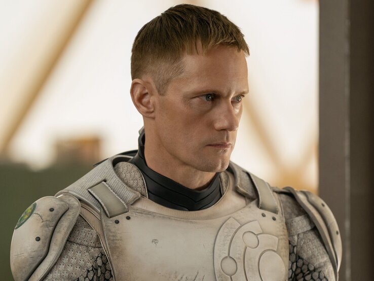 Alexander Skarsgård Murderbot Interview Alexander Skarsgård mit kurzen blonden Haaren und ernster Miene trägt als "Murderbot" einen futuristischen Raumanzug und blickt entschlossen in die Ferne.