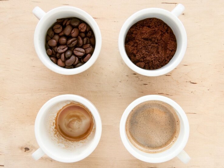 Kaffee-Raetsel Aufmacher Vier weiße Tassen zeigen Bohnen, Pulver, frischen Kaffee und Kaffeereste als Phasen der Kaffeezubereitung von oben.