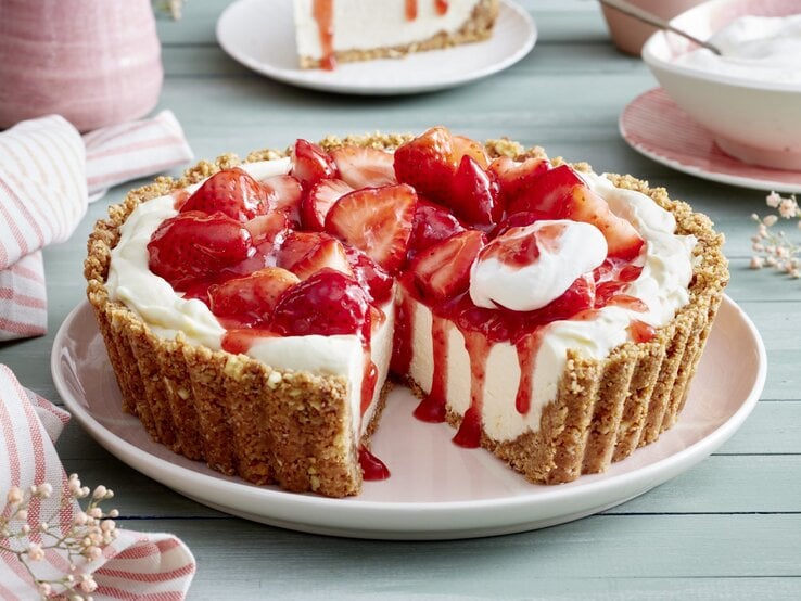 Erdbeer-Zitronen-Pie auf einem rosa Servierteller auf hellgrünem Hintergrund. Auf dem Foto hinten rosa Geschirr verteilt.