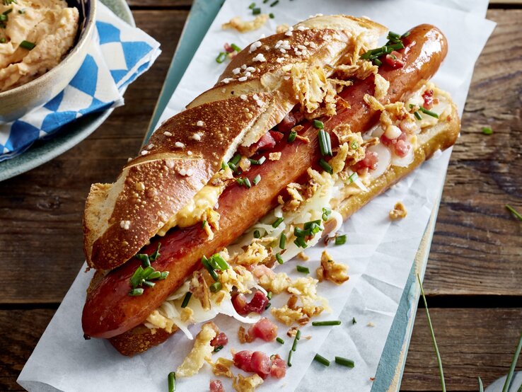 Hol dir ein Stück Bayern nach Hause! Unser Hotdog auf bayerische Art vereint die besten regionalen Zutaten in einem unwiderstehlichen Snack – perfekt für jede Gelegenheit! Hotdog auf bayerische Art auf weißem Papier auf hölzernem Hintergrund.