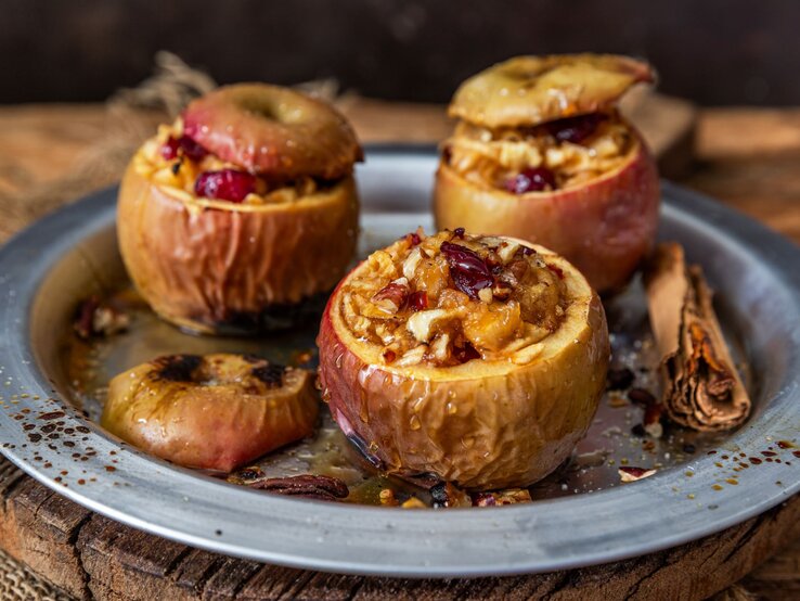 Bratapfel Airfryer Drei ofengebackene Äpfel mit nussiger Füllung und Cranberries in einem Metallteller, dekoriert mit Zimtstangen auf rustikalem Untergrund.