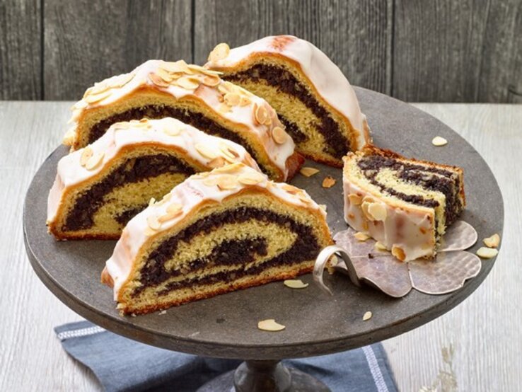 Frisch gebacken und voller Geschmack: So wird dein Mohnstollen zum Star auf jeder Winterparty – probier’s aus! Mohnstollen auf einem schwarzen Tortenteller auf hölzernem Hintergrund.