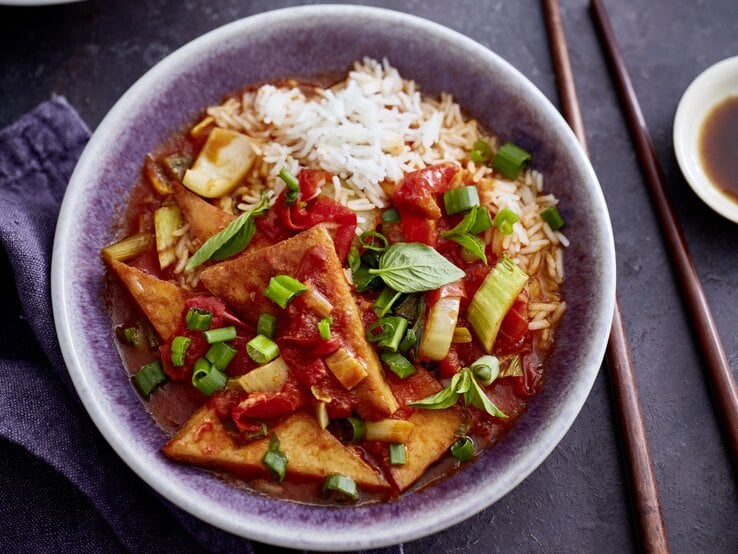 Tofu süßsauer mit Pak Choi und Paprika in einer grauen Schüssel auf grauem Hintergrund. Rechts von der Bowl sind Stäbchen. 