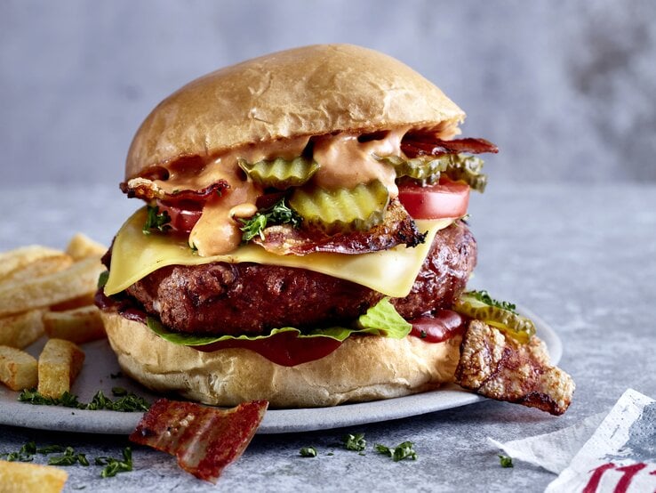 Kompromisslos guter cheesy Böhnchenburger auf einem Teller mit Pommes angerichtet. Der Hintergrund ist grau.