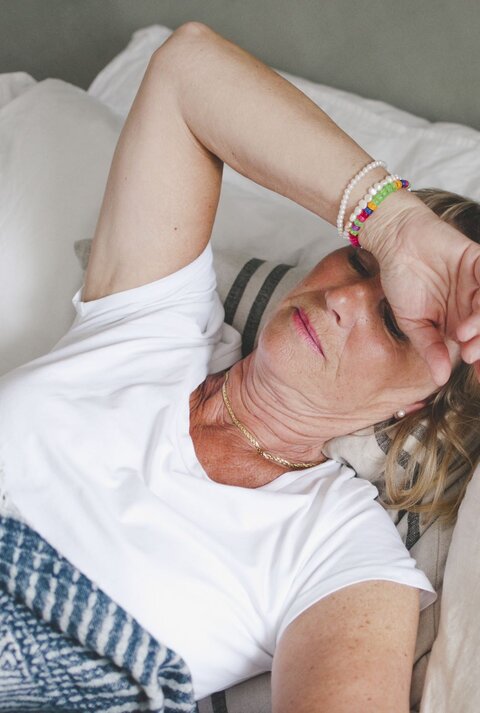 Zu sehen ist eine Frau mittleren Alters im Bett liegend, der sichtlich zu warm ist.