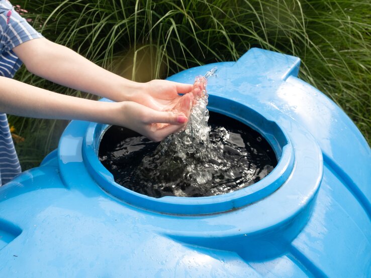 Regentonne in blau, mit Händen im Wasser