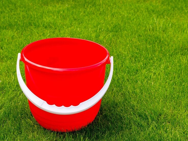 Plastikeimer Upcycling Ein leerer, knallroter Plastikeimer mit weißem Henkel steht auf dichtem, frisch gemähtem, sattem grünen Rasen.