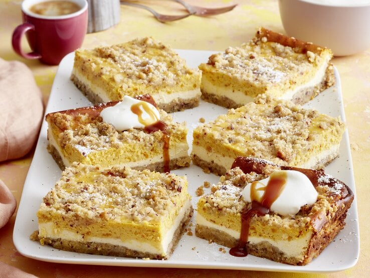 Draufsicht auf sieben Stücke des Kürbis-Streuselkuchen auf einer Kaffeetafel.