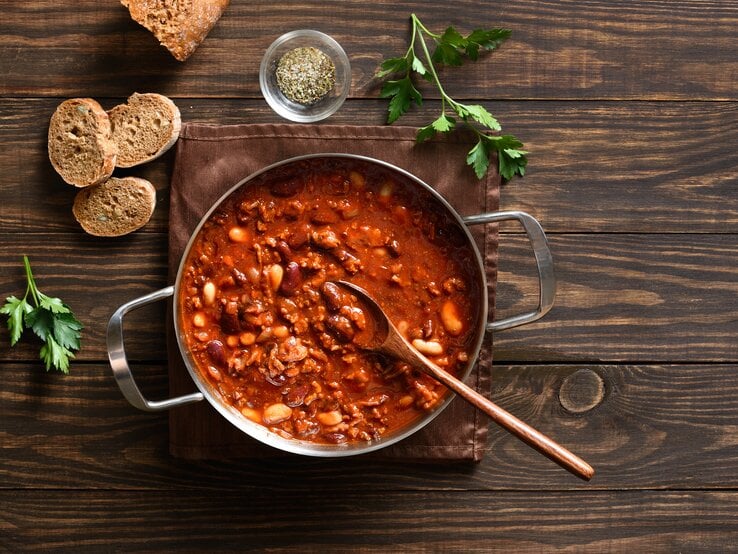 Deftige Cowboy Bohnen mit Hackfleisch und Bohnenmix in roter Sauce, angerichtet im Topf auf rustikalem Holztisch.