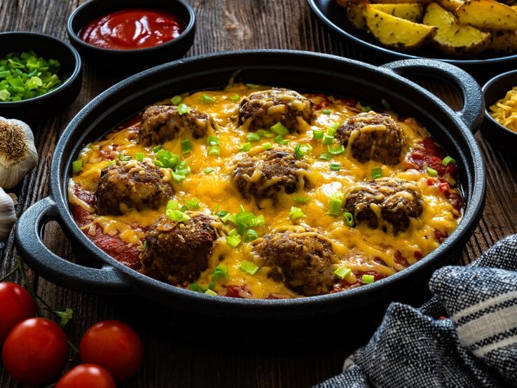Überbackene Cowboy Fleischbällchen mit geschmolzenem Käse und grünen Zwiebeln in Tomatensauce, serviert auf rustikalem Holztisch.