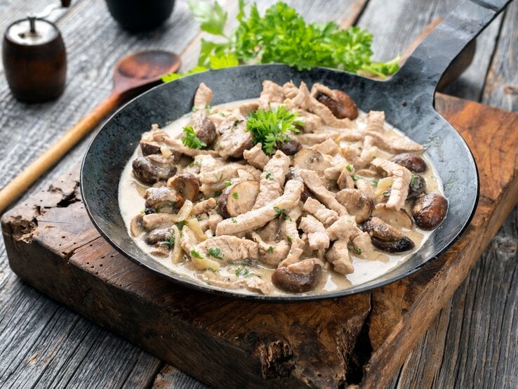 Zürcher Geschnetzeltes in gusseiserner Pfanne auf Holzbrett. 