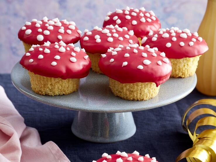 Frontalansicht von sechs Glückspilz-Muffins auf einer Etagere und einem auf einer vergoldeten Untertasse.