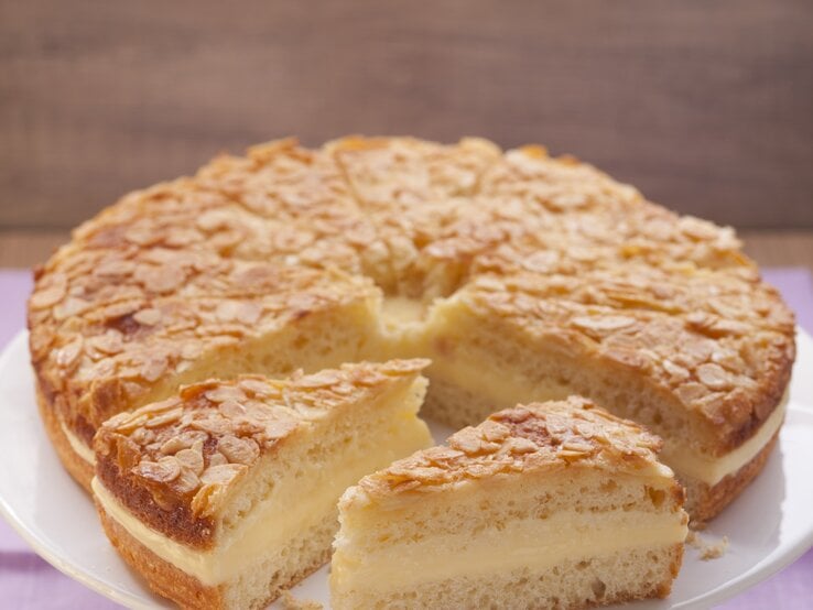 Draufsicht auf einen angeschnittenen Bienenstich auf einer weißen Etagere, davor ein Stück des Kuchens.