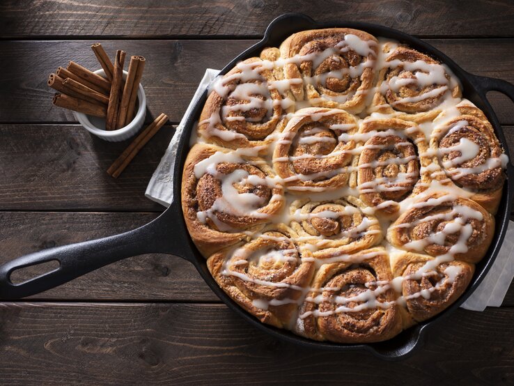 Draufsicht auf einer gusseiserne Pfanne mit saftigen Zimtschnecken, die mit einem Frischkäse-Frosting garniert sind.