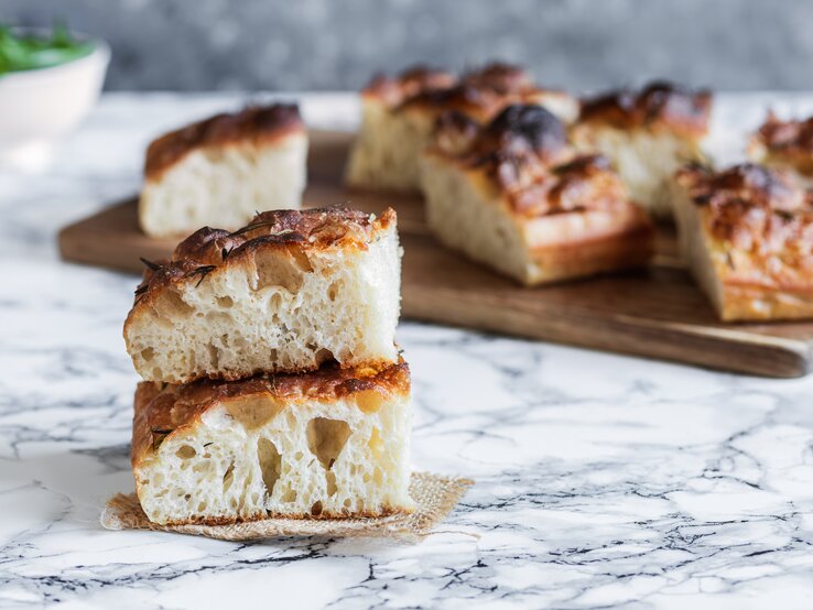 Nahaufnahme von zwei Stück fluffiger Focaccia, im Hintergrund weitere Focacciastücke.