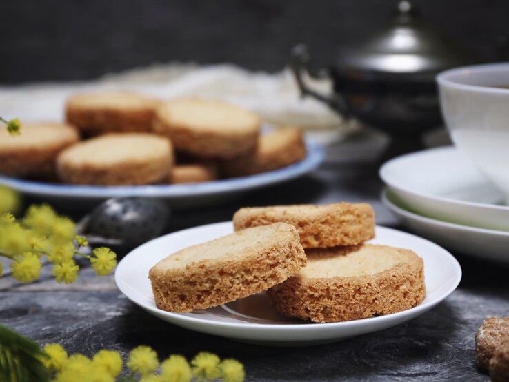 Drei Palets bretons auf einem runden, kleinen Teller / Hintergrund sechs der kekse auf einem runden Teller / Teekanne aus Metall / Frontalsicht