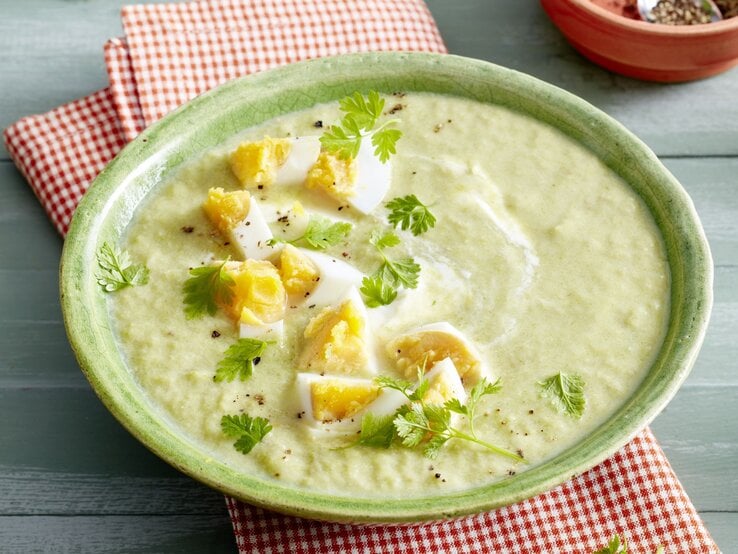 Eine Schale mit cremiger Lauch-Champignon-Suppe, verziert mit gehacktem hartgekochtem Ei und frischem Kerbel. Die Suppe hat eine hellgrüne Farbe mit weißen Joghurtwirbeln.