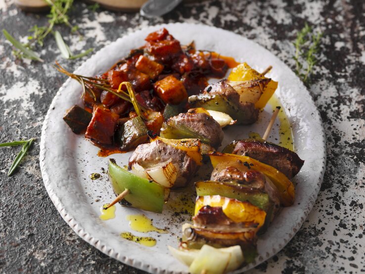 Schräge Draufsicht auf einen weißen Teller mit den Schaschlikspießen mit Gemüse.