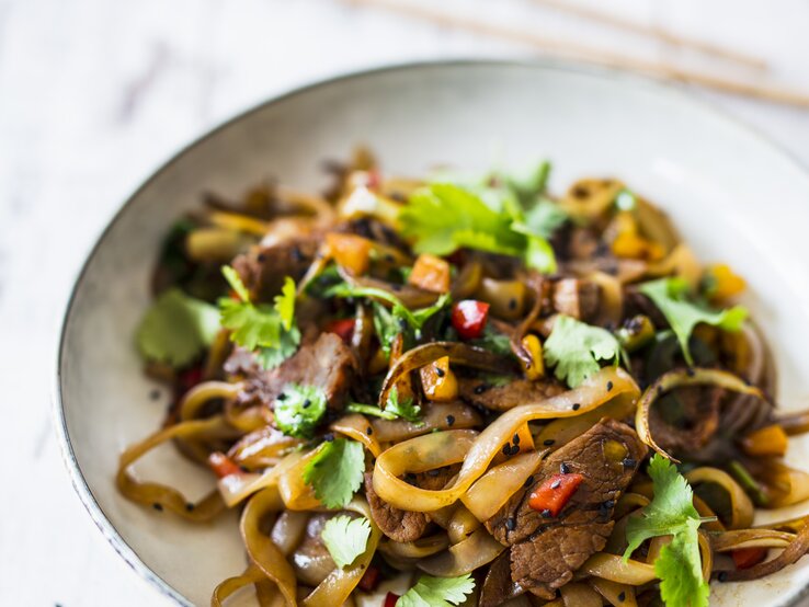 High Protein Nudeln mit Schweinefilet und Paprika in einer weißen Prozellanschüssel vor weißen Hintergrund.