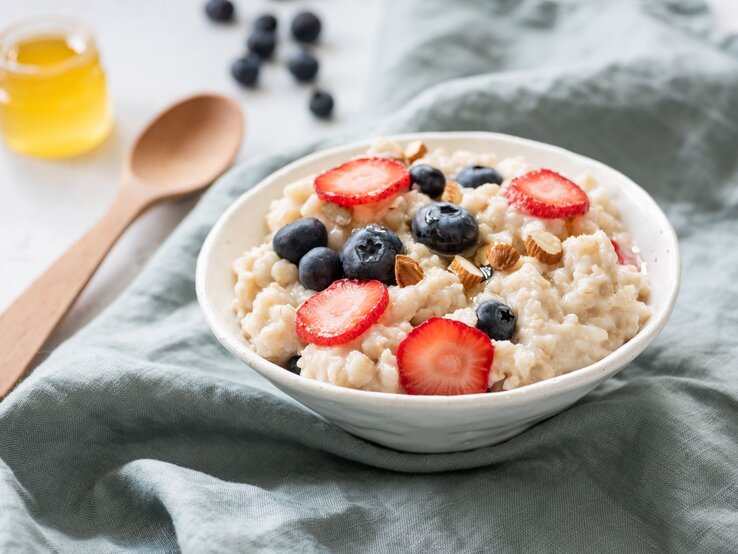 Cremiges Porridge in einer Schale mit Erdbeeren, Blaubeeren, Mandeln und Honig.