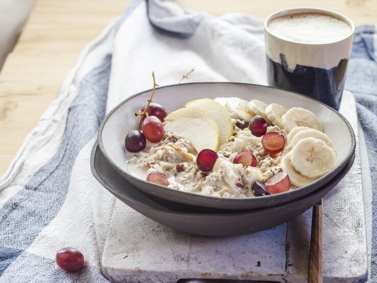 Bircher Müsli mit Haferflocken, Banane, Trauben und Apfelscheiben in einer Schale.