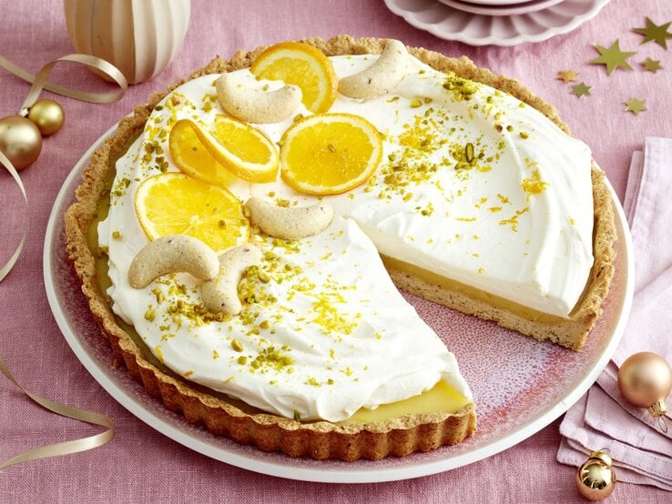 Orangen-Nuss-Tarte mit Sahnecreme, Orangenscheiben und Nüssen auf einer Tortenplatte.