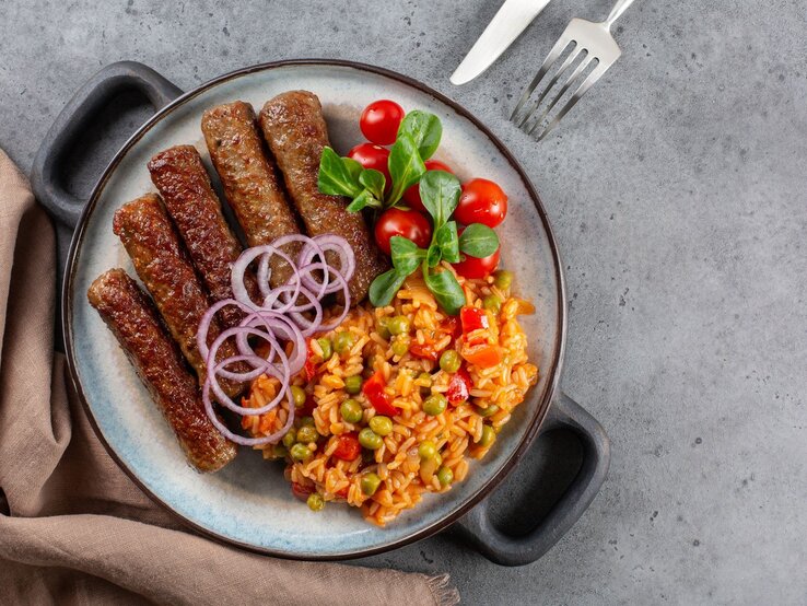 Djuvec-Reis mit Cevapcici auf Teller. 