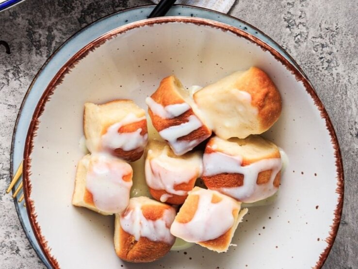 Vegane Buchteln mit Aprikosenmarmelade und Vanillesauce in einer Schüssel auf grauem Untergrund.