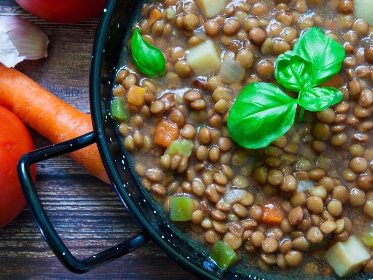 Klassischer Linseneintopf mit Basilikumblätternobendrauf / daneben frische Möhren / Draufsicht, schräg