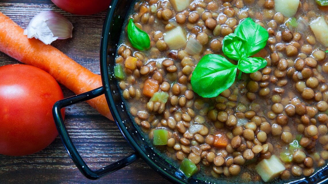 Klassischer Linseneintopf mit Basilikumblätternobendrauf / daneben frische Möhren / Draufsicht, schräg