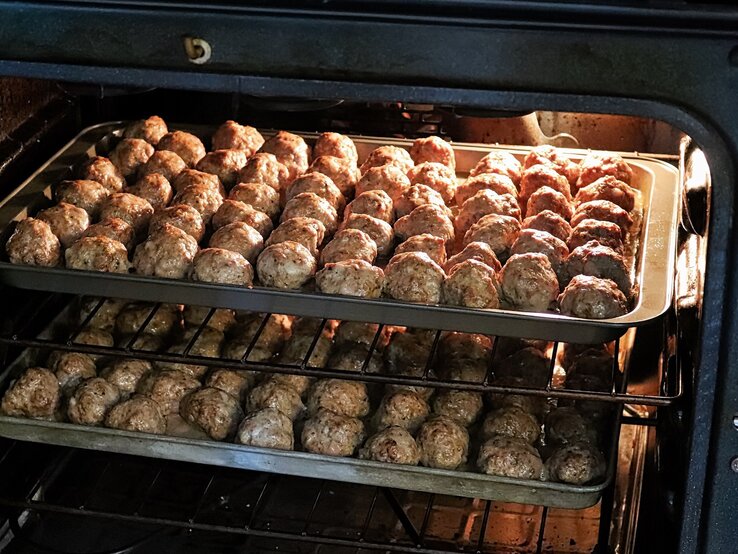 Frikadellen im Backofen zubereiten / zwei Bleche mit Hackbällchen / Draufsicht, schräg
