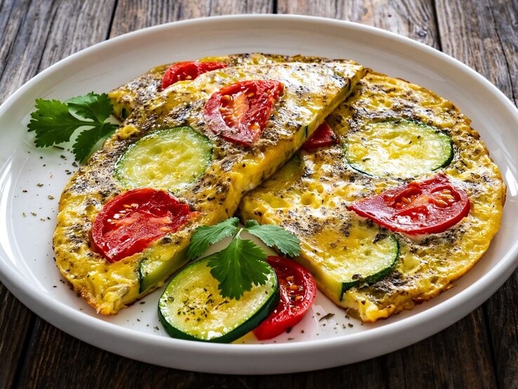 zwei halbierte Zucchini-Pfannkuchen mit Tomaten  / runder Teller / frische Petersilie / Draufsicht, schräg